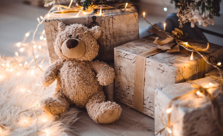 Teddy bear and presents underneath a Christmas tree with fairy lights