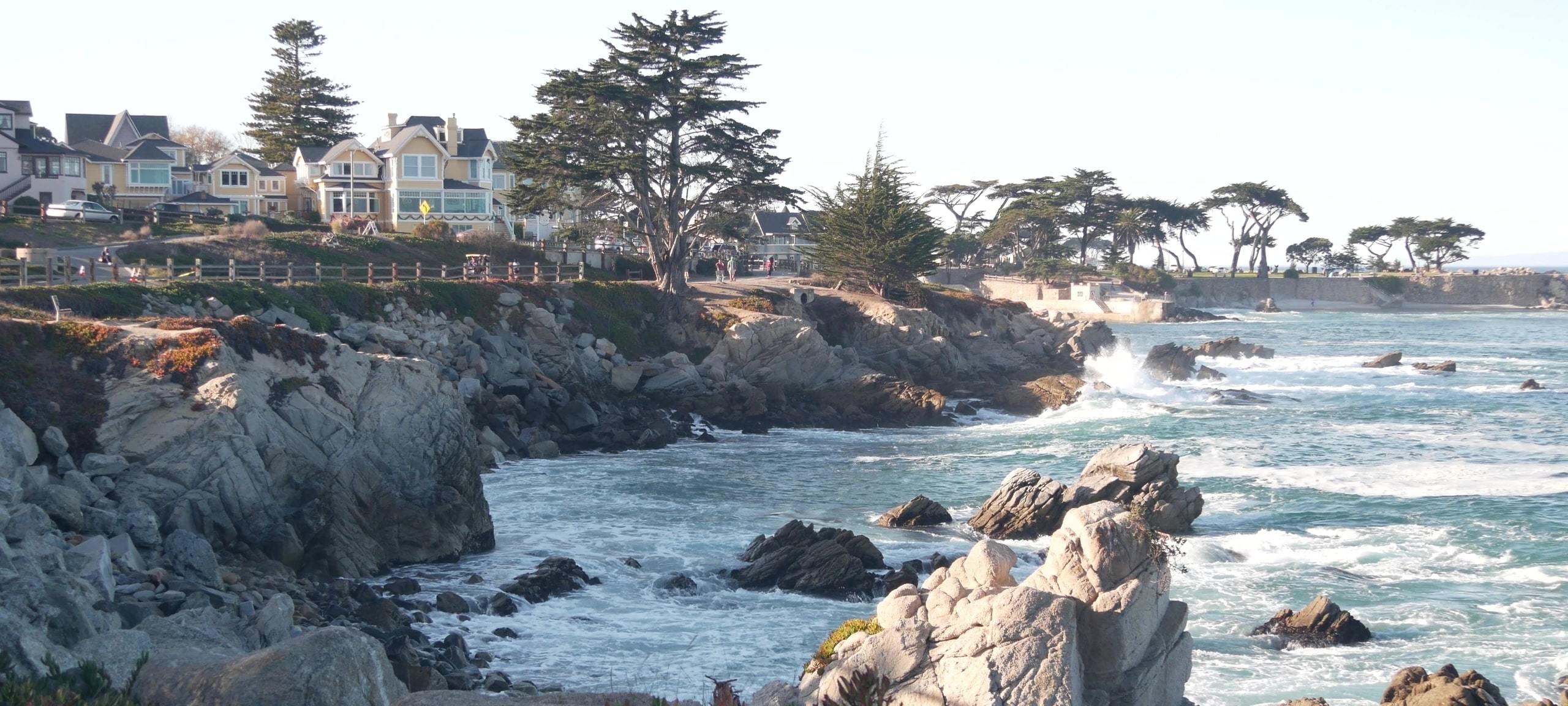 Waves crashing on rocky Monterey Bay area cliffs with homes on shore