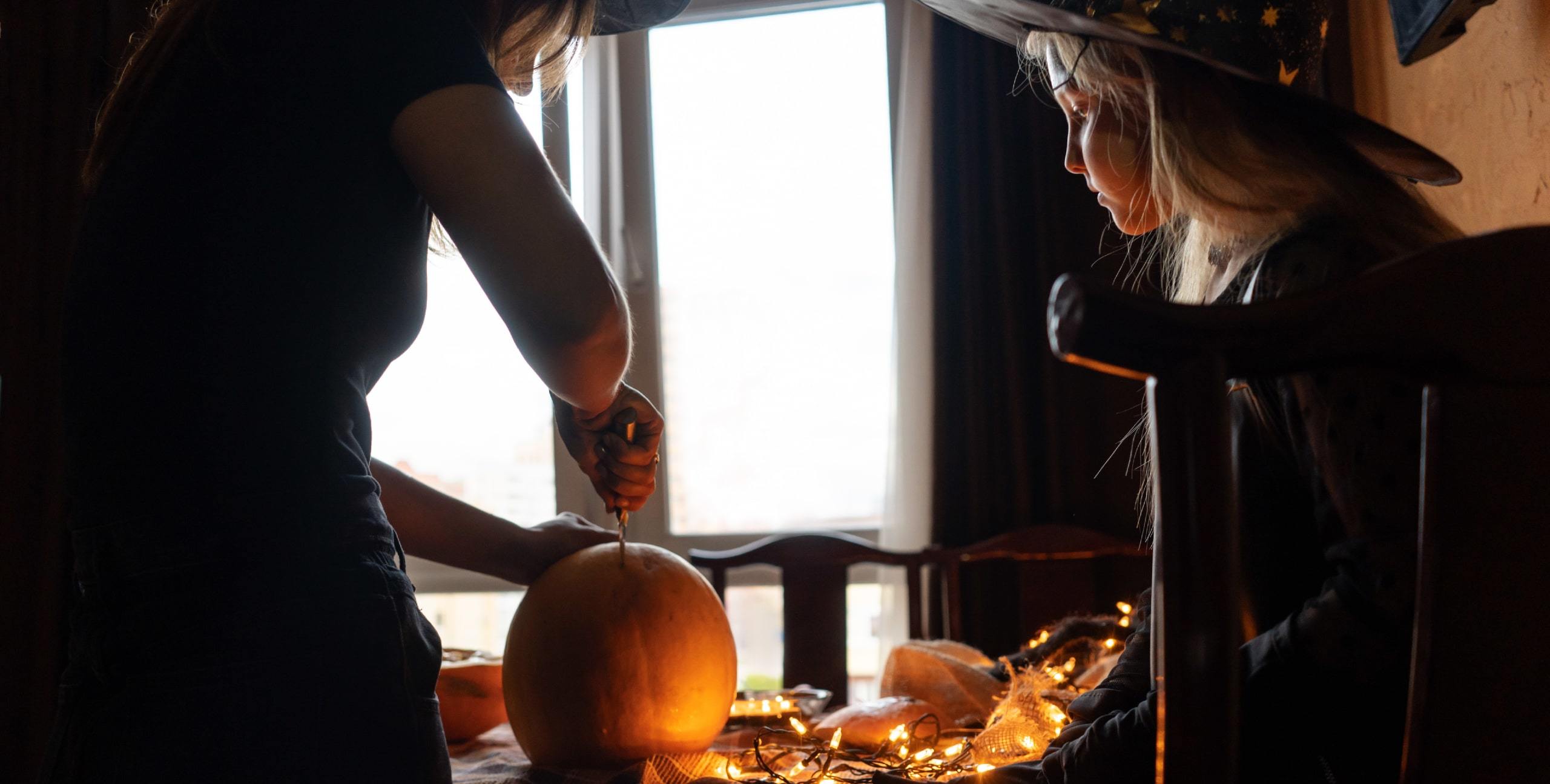 Mother and daughter in Halloween costumes carving a pumpkin