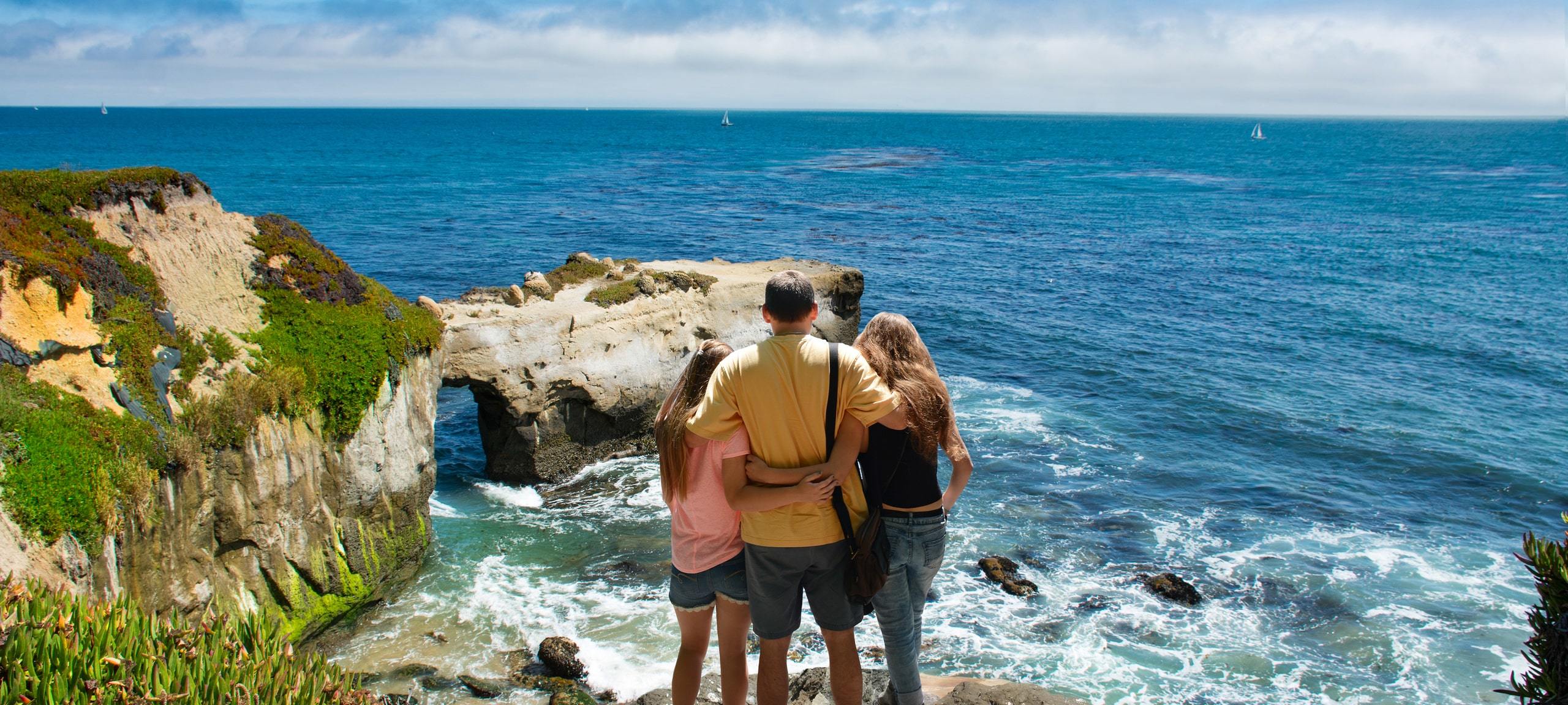 Family trio overlooking the Santa Cruz waves from the rocks above on a sunny day