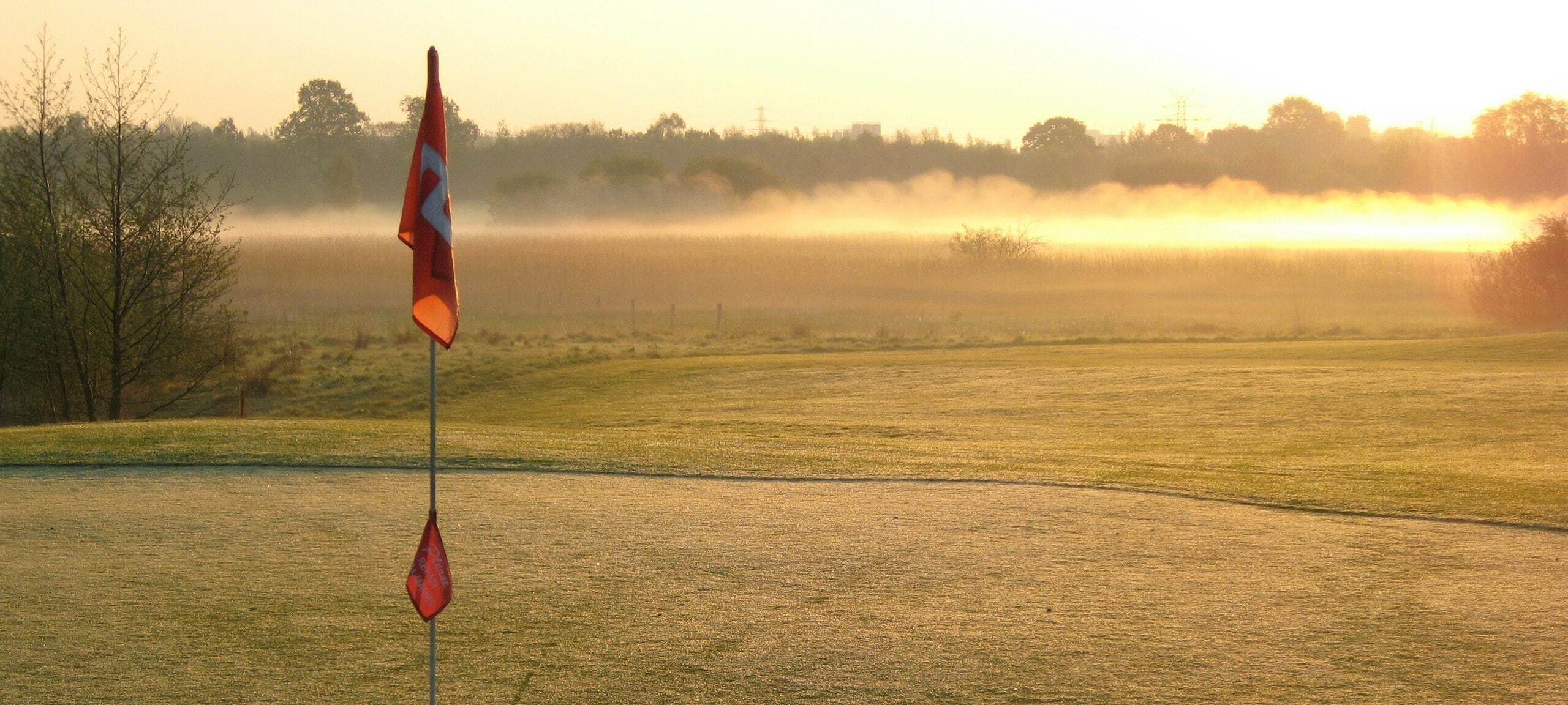 Flag on golf course with dew and fog of the early morning. Photo by Michael Jasmund on Unsplash