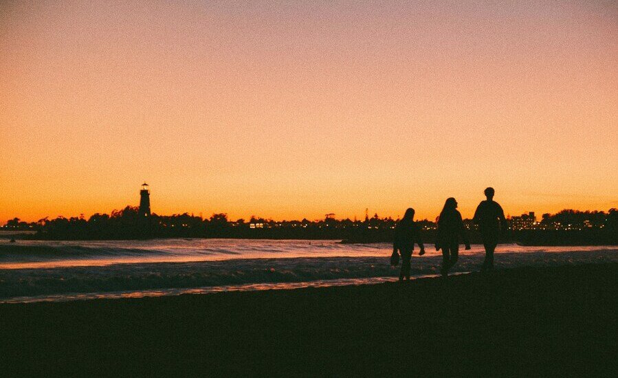 Silhouettes of people walking along Santa Cruz beach during sunset. Photo by Chris Leipelt on Unsplash